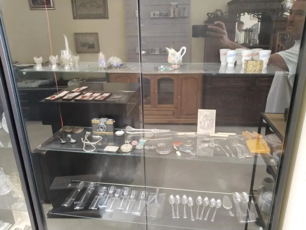 A cabinet displaying a collection of antique items at Antiques & Art Gallery in Varna, including silverware, vintage cameras, and decorative treasures.