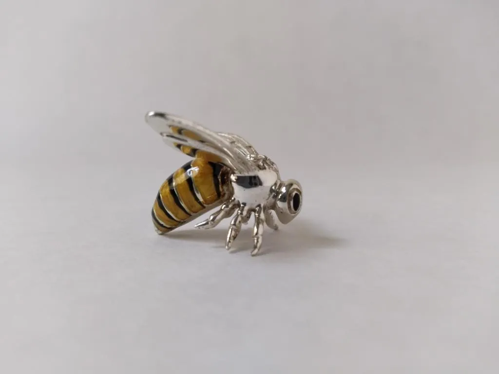 This is a Saturno Sterling Silver and Enamel Wasp Figurine. The figurine is crafted from sterling silver and features intricate details, including the wings and legs. The body of the wasp is decorated with vibrant enamel in yellow and black stripes, closely mimicking the natural colors of a wasp. The craftsmanship showcases the precision and artistry typical of Saturno's work.