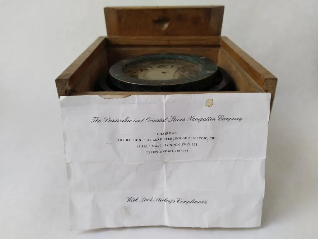 The Sestrel compass, still nestled in its original wooden box, accompanied by a note from The Peninsular and Oriental Steam Navigation Company. The folded note, likely a gift from Lord Sterling, adds significant historical value and intrigue to this already rare nautical instrument.